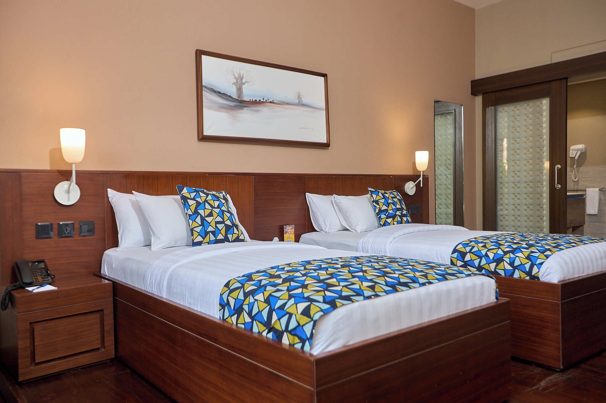 A hotel room with two beds, a nightstand with a phone, and a painting on the wall.