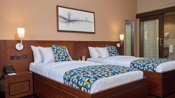 A hotel room with two beds, a nightstand with a phone, and a painting on the wall.