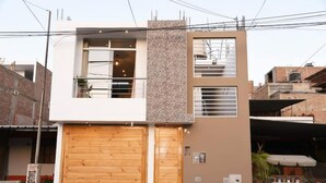 Una casa moderna de dos pisos, con puerta de garaje de madera, balcón y una ventana pequeña.