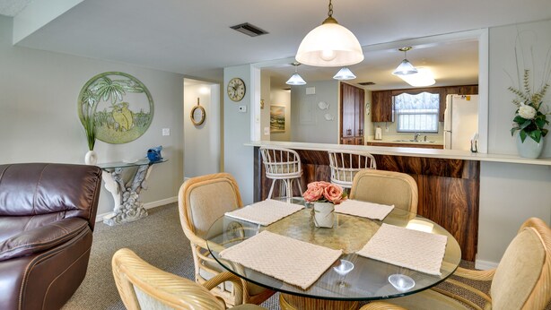 A dining area with a glass table, cushioned chairs, and a hanging light fixture. - Daytona Beach Shores Condo Rental: Walk to Beach! (Daytona Beach Shores)