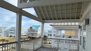 Une terrasse en bois avec une balustrade blanche, donnant sur une plage bordée de maisons.