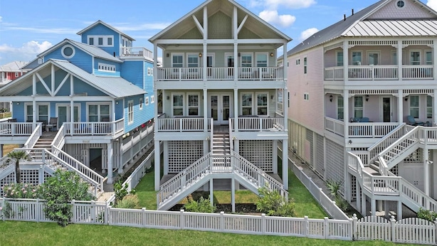 Une rangée de maisons de plage à plusieurs étages, dotées de balcons, d’escaliers et d’une clôture blanche en bois.