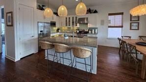 Une cuisine moderne dotée d’un îlot central, de tabourets de bar, de luminaires suspendus et d’un revêtement de sol en bois.