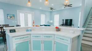 Een moderne keuken met witte kasten en blauwgroene accenten, een eetgedeelte met houten stoelen, en een trap die naar een ander niveau leidt.