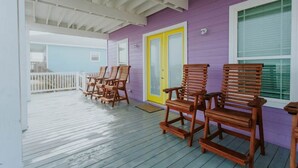 Een overdekt terras met houten stoelen en een deur met geel-witte sierlijsten.