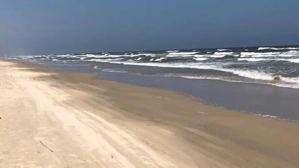 Een strand met een brede zandvlakte en golven die op het strand breken.