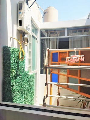 A window with a view of a building's exterior, including a white wall, a window with a blue frame, and a green hedge.