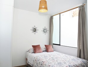 A bedroom with a bed, two wall-mounted wall sconces, a window with curtains, and a hanging light fixture.