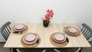 Ruokapöytä on katettu vaaleanpunaisilla lautasilla, aterimilla ja punotuilla aluslautasilla, ja sen ympärillä on tuoleja.