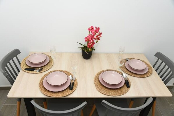 A dining table set with pink plates, cutlery, and woven placemats, surrounded by chairs.