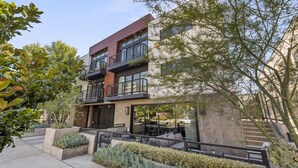 A modern multi-story building with balconies, outdoor seating, and a landscaped courtyard.