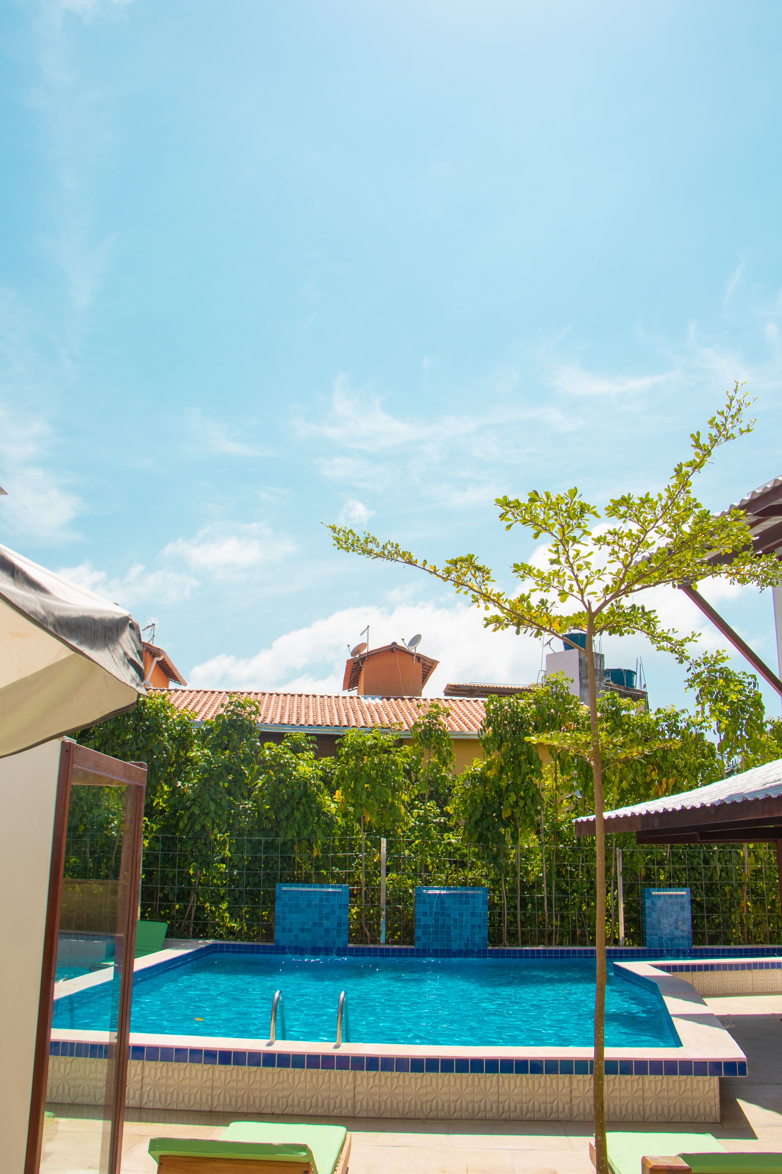 A swimming pool with a tiled edge, surrounded by greenery and buildings.