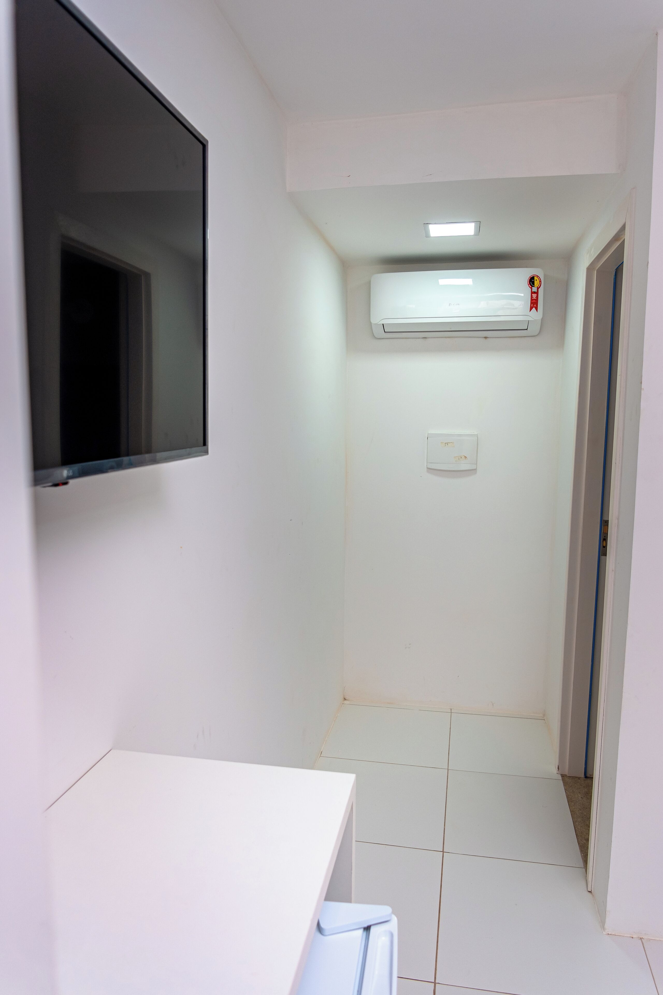 A narrow hallway with white walls, a mounted air conditioner, a light switch, and a door at the end.