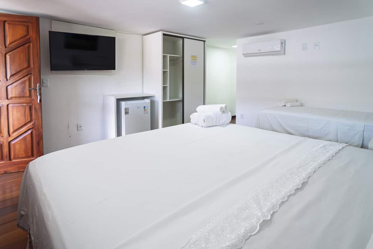 A hotel room with a large bed, a wardrobe, a television, a small refrigerator, and a bathroom with a towel rack.