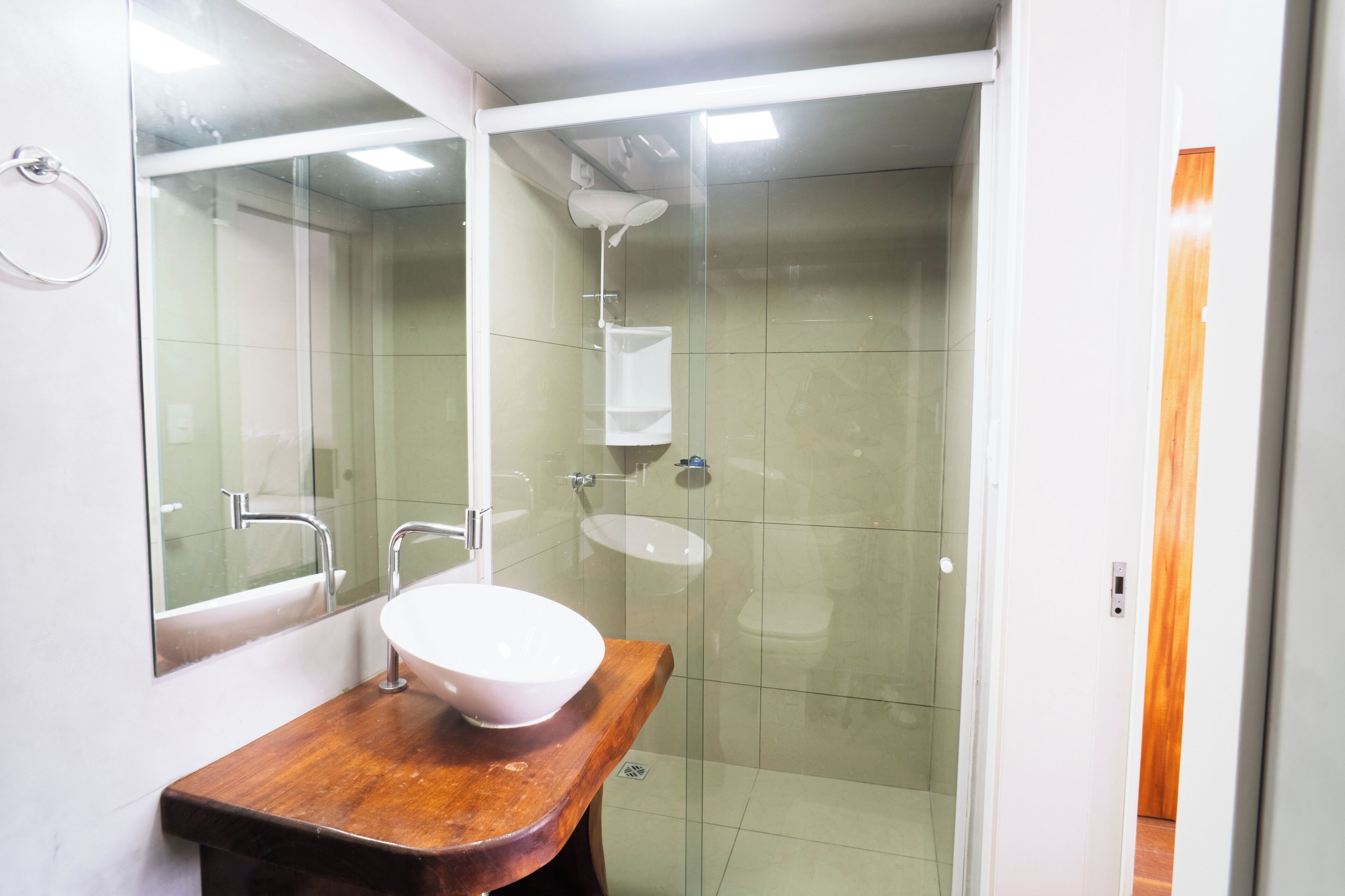 Une salle de bain avec un meuble-lavabo en bois, un lavabo blanc et une douche séparée par des parois en verre.