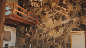 Una habitación acogedora con pared de piedra, vigas de madera en el techo, una cama, un sofá y un comedor con chimenea de piedra.