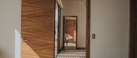 A bedroom with a bed, a wooden wardrobe, and a view of a hallway with a chair.
