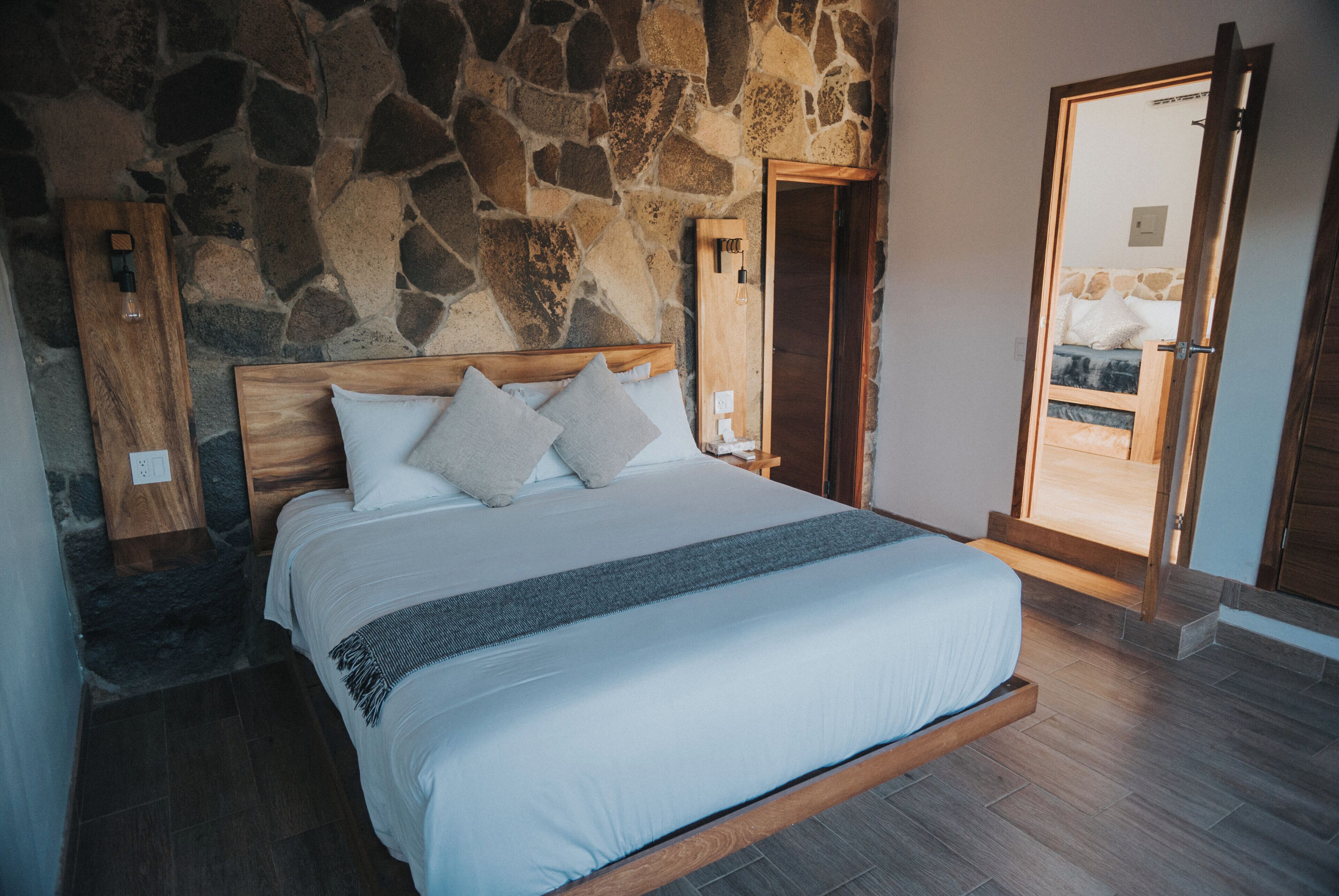 Ein Schlafzimmer mit Steinwand, Holzbettgestell und einer Tür, die auf einen Balkon führt.