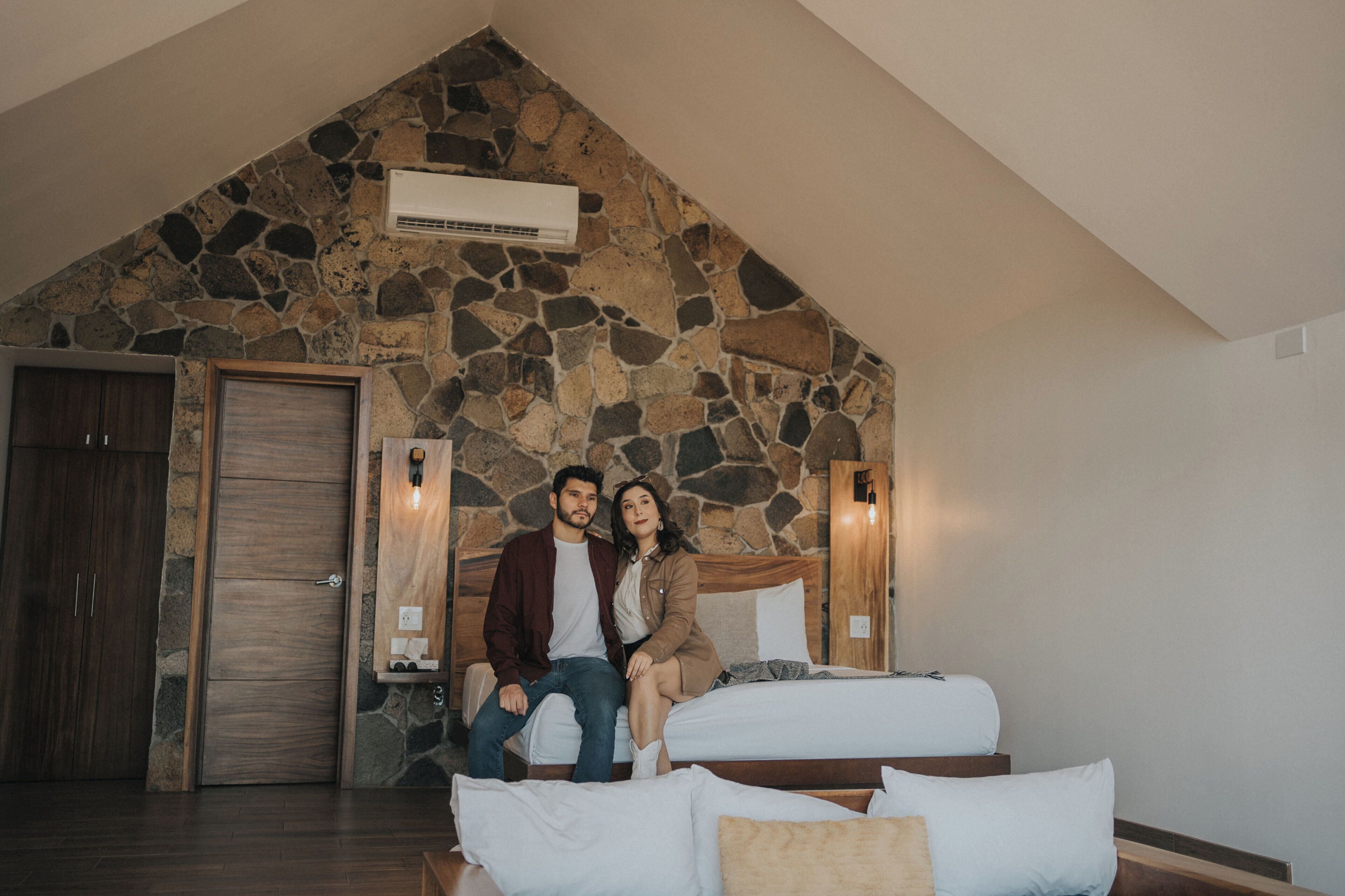 Una habitación con pared de piedra, una cama, una puerta de madera y un equipo de aire acondicionado.