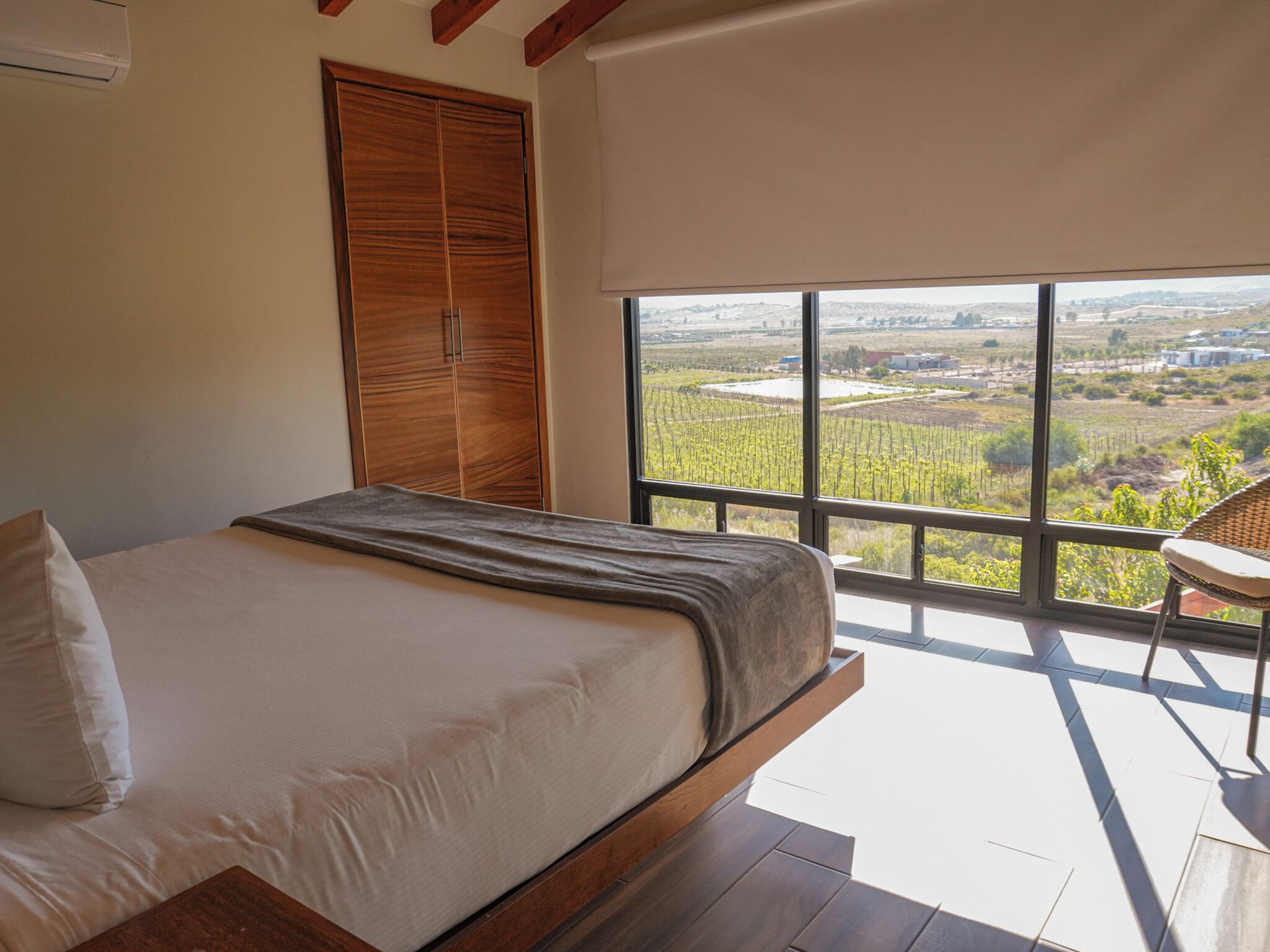 Un dormitorio con cama, armario de madera y vistas a viñedos a través de amplias ventanas.
