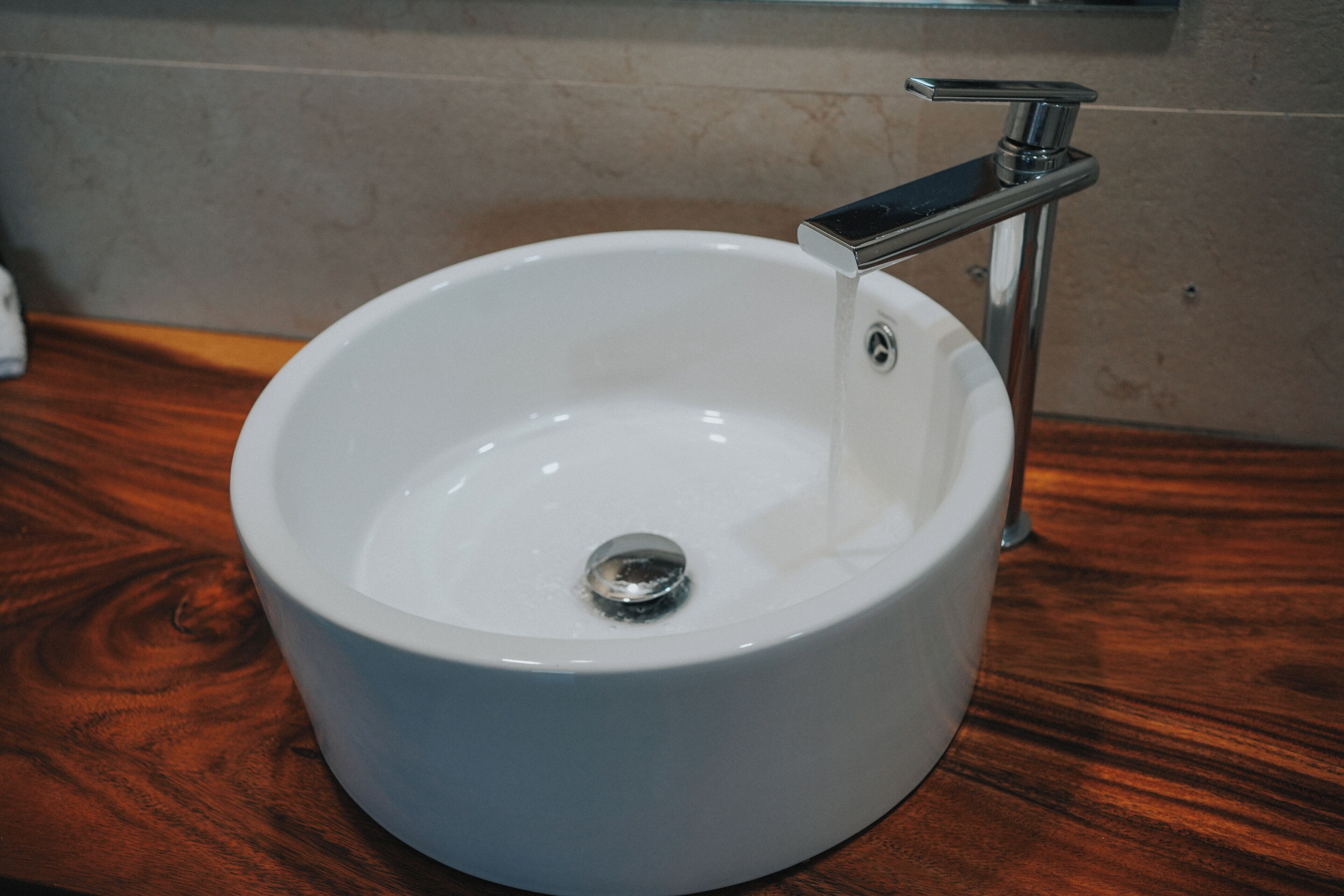 A white ceramic sink with a chrome faucet, mounted on a wooden countertop.