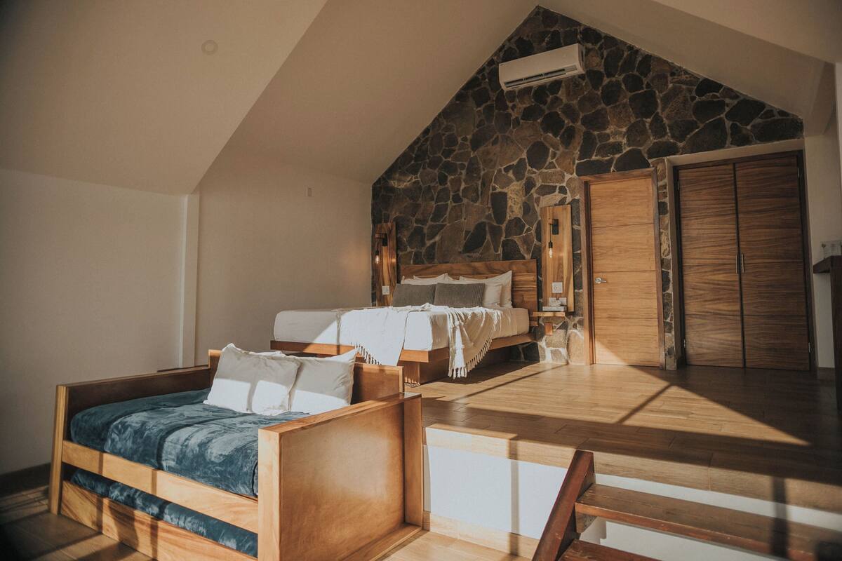 Un dormitorio con techo inclinado, pared de piedra, cama de madera y un armario.