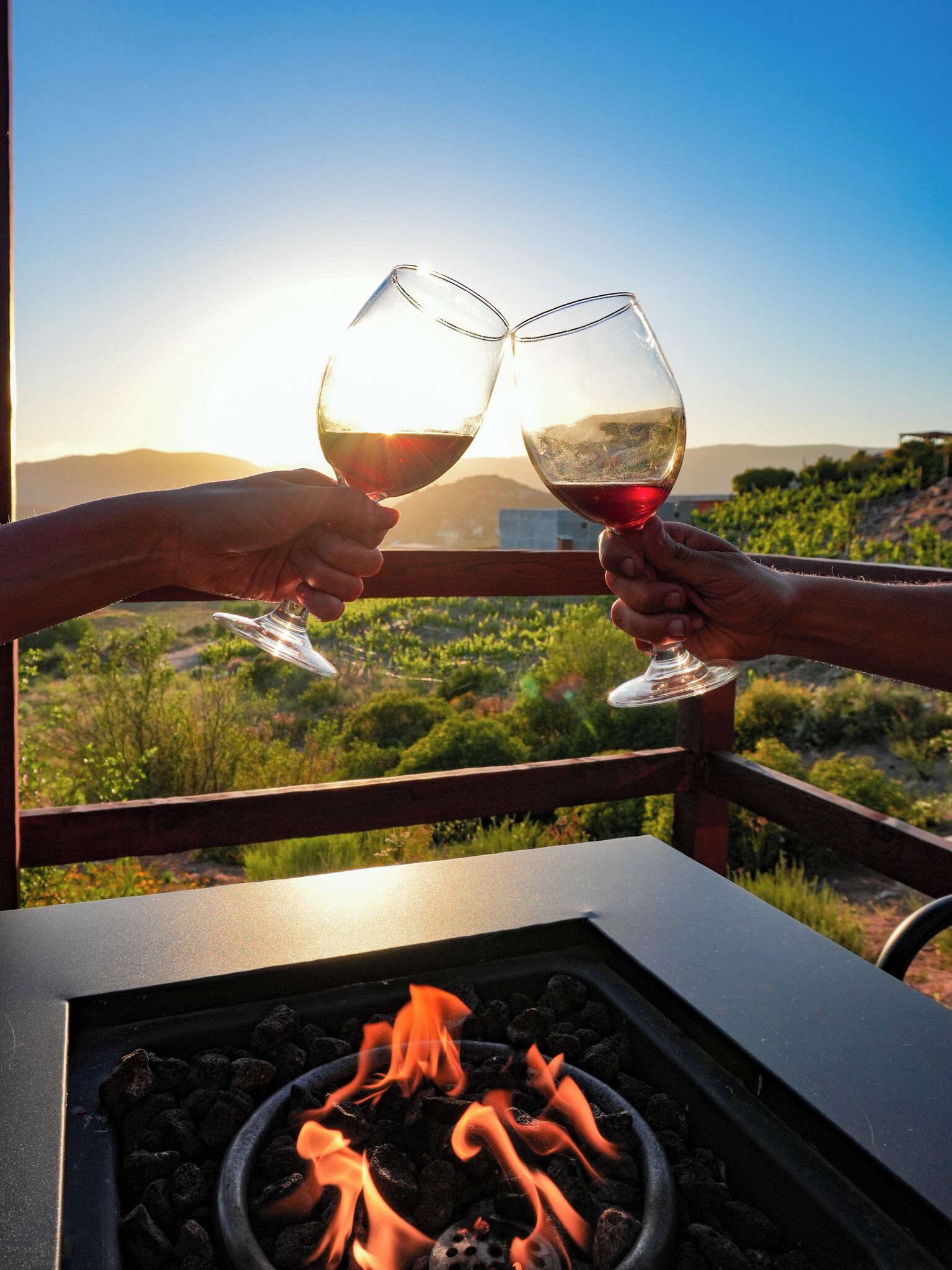 Two people toasting with wine glasses, a fire pit, and a scenic outdoor view.