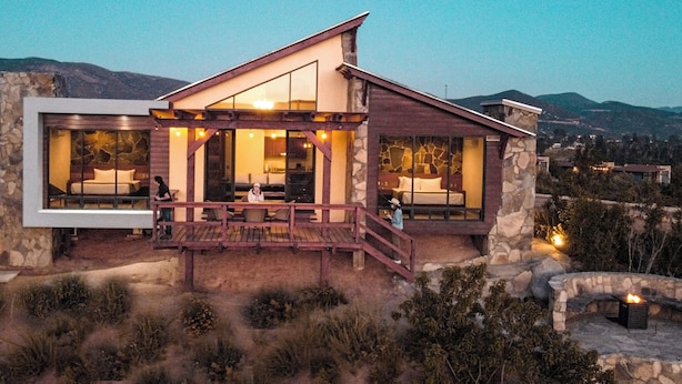 Una casa moderna con amplios ventanales, fachada de piedra y terraza de madera.