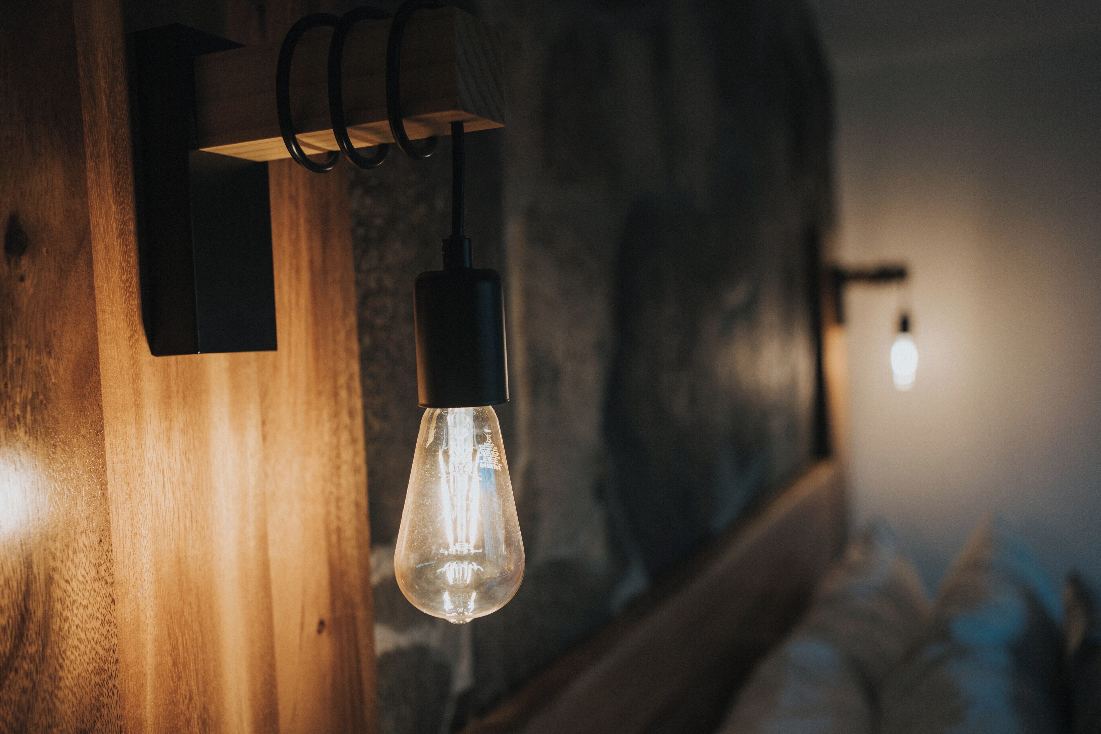 Una lámpara con bombilla de vidrio transparente, pared de madera y una luz cálida.