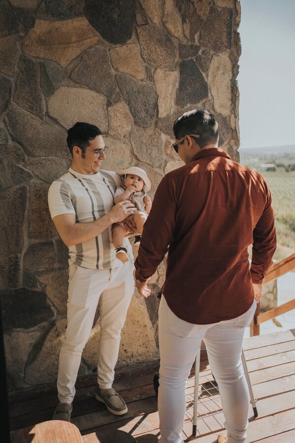 A man holding a baby against a stone wall, with another man standing nearby.