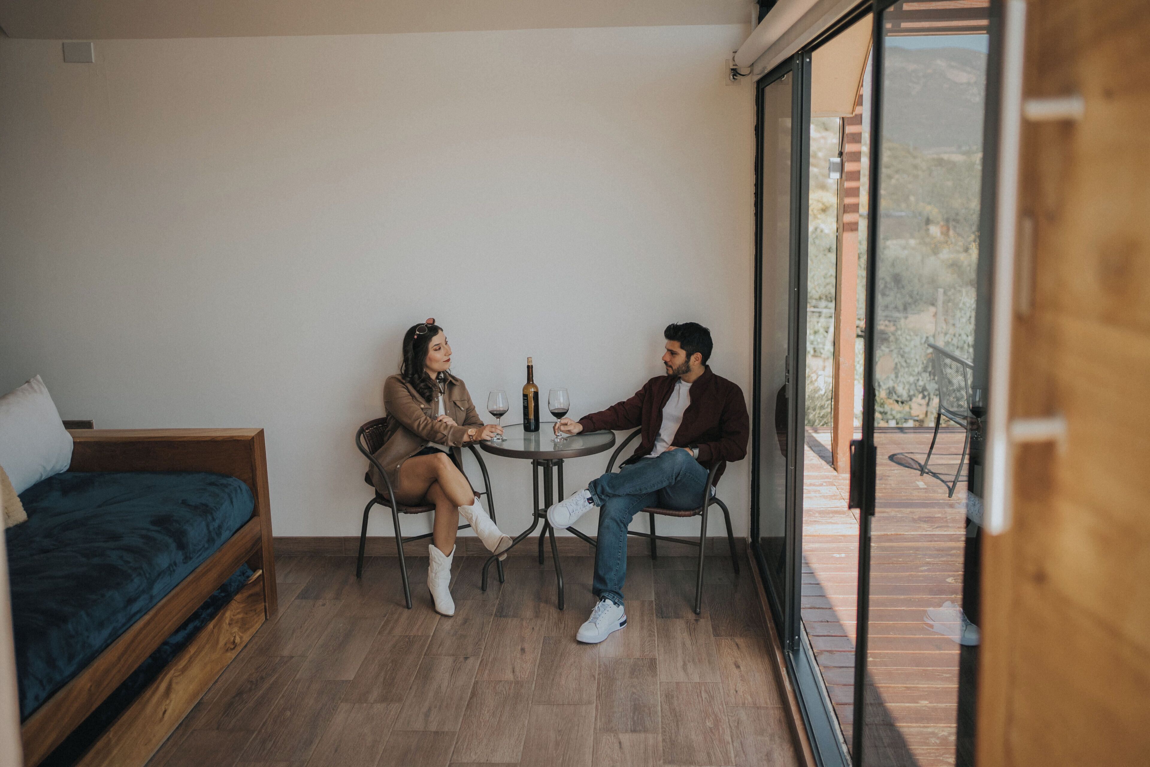 A room with a bed, a table with two chairs, and a view through a glass door.
