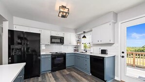 Una cucina moderna con mobili bianchi, un frigorifero nero, un forno a microonde ed una lavastoviglie.