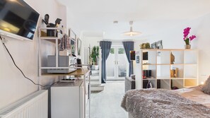 Una sala de estar moderna con una televisión de pantalla plana, una cocina con electrodomésticos, un sofá y una estantería.