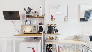 Eine Küchenzeile mit Mikrowelle, Wasserkocher und Kaffeemaschine auf einer weißen Arbeitsplatte.