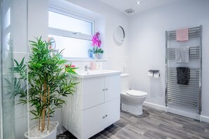 A modern bathroom with a white vanity, a toilet, a towel rack, and a potted plant.