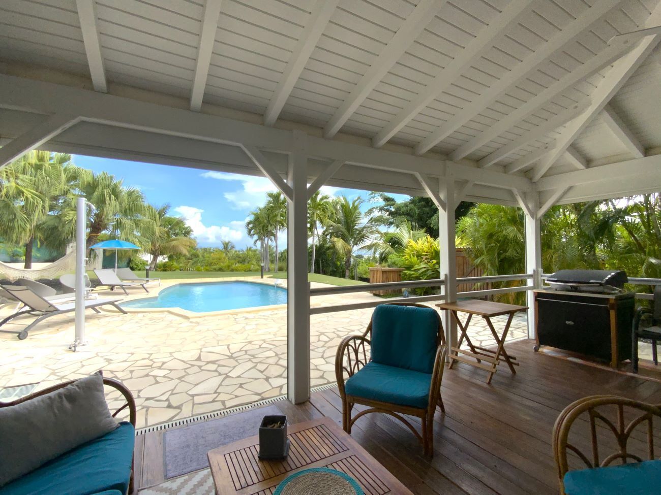 A covered outdoor area with a pool, lounge chairs, and a grill.