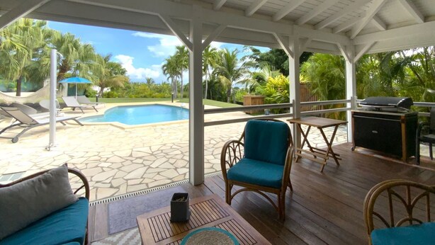 Uma área externa coberta com piscina, espreguiçadeiras e churrasqueira.