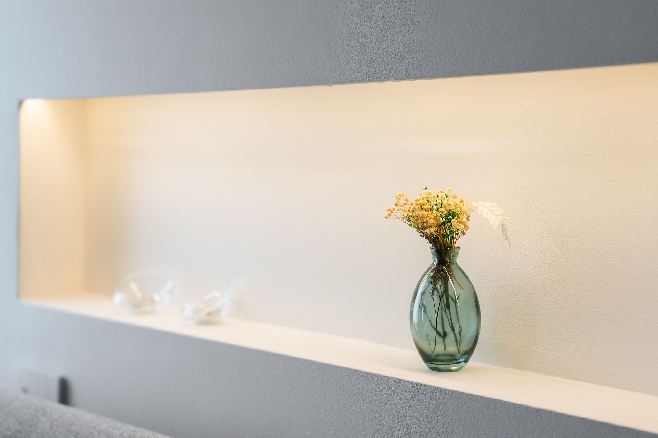 Eine Vase mit Blumen auf einem Regal an einer Wand.