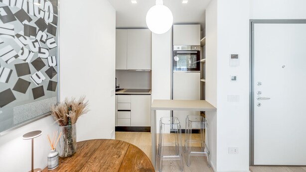 Una cocina moderna con armarios blancos, una mesa de comedor de madera y una lámpara colgante.