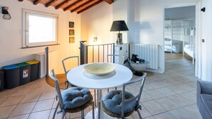 Un coin repas avec une table ronde, des chaises et un vase servant de centre de table. On y trouve également une fenêtre, une lampe et un radiateur.