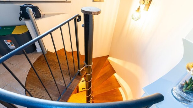 Un escalier en colimaçon avec une rampe en métal, des marches en bois et un luminaire fixé au mur.