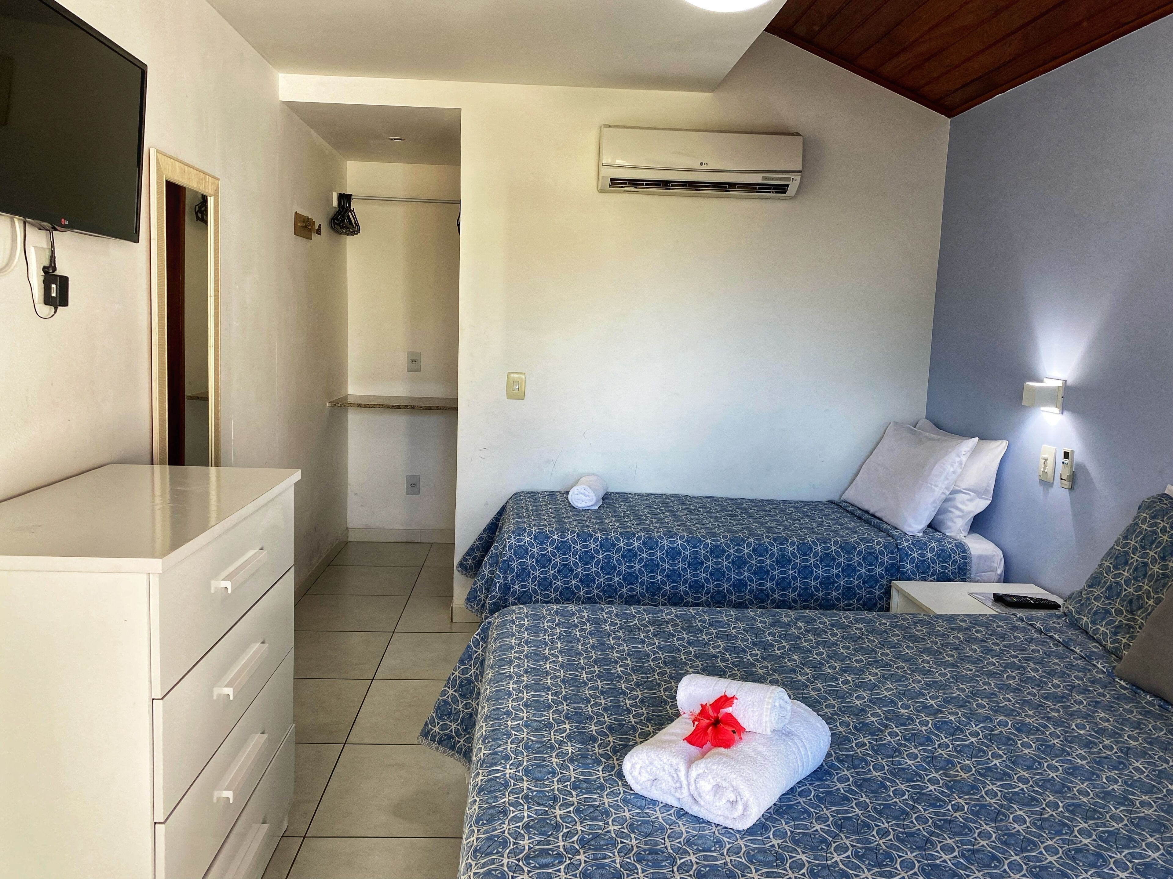 A hotel room with a bed, a TV, an air conditioner, and a bathroom visible through an open door.