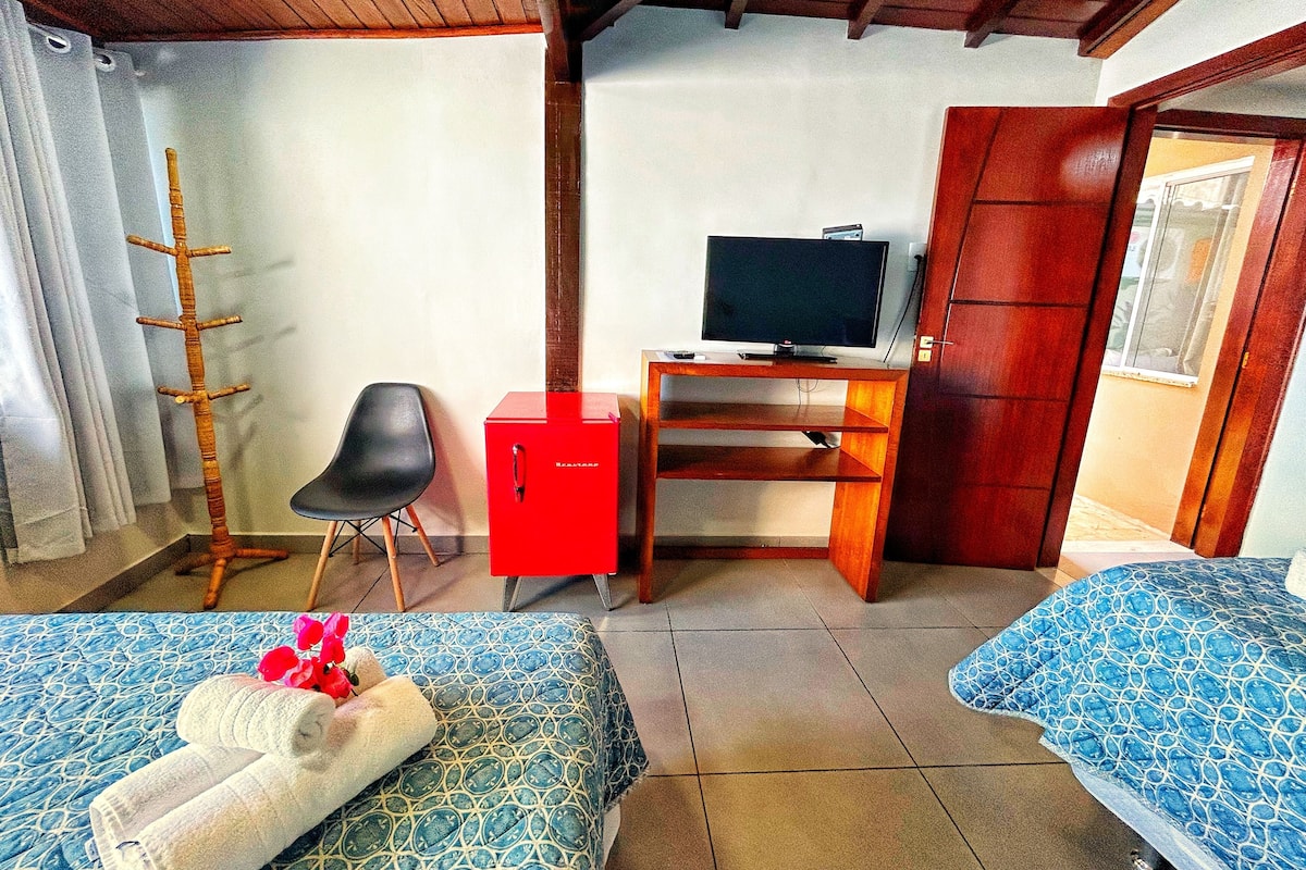 Ein Zimmer mit zwei Betten, einem Schreibtisch mit Fernseher, einem Sessel und einem Kleiderschrank.