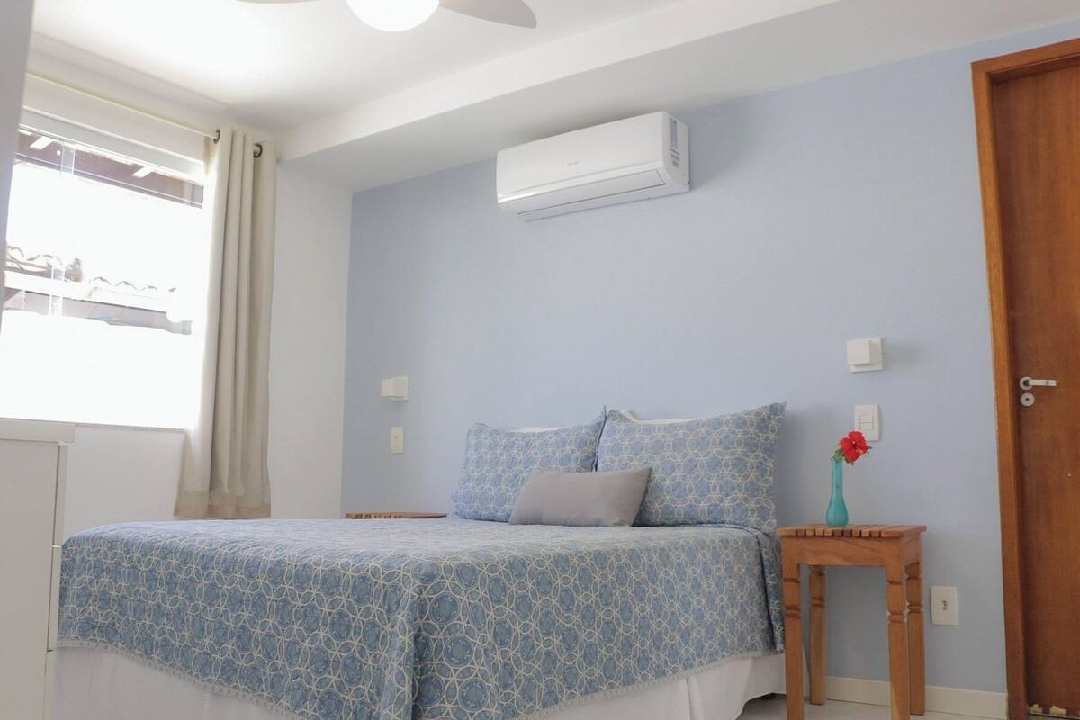 Ein Schlafzimmer mit einem Bett, einem Nachttisch, einer Blumenvase, einer Klimaanlage und einer Tür.