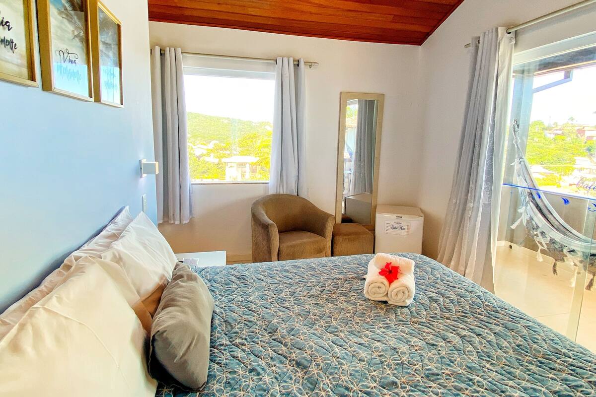 Ein Schlafzimmer mit Bett, Stuhl, Spiegel und einem Balkon mit Blick.