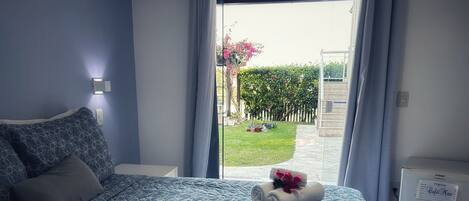 Un dormitorio con cama, mesita de noche, ventana con cortinas y vista a un jardín.