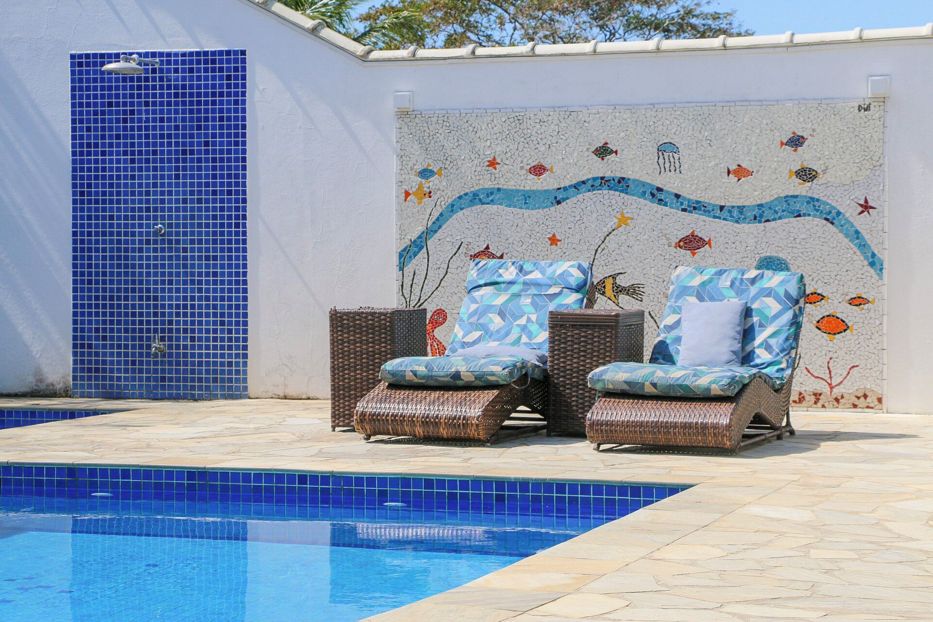 A pool area with two wicker lounge chairs and a mosaic wall.