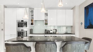 Une cuisine moderne avec des meubles blancs, un îlot central doté de tabourets et des appareils électroménagers en acier inoxydable.