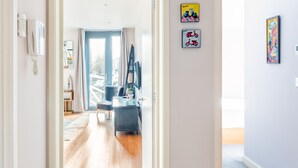 Un couloir au plancher de bois menant à une pièce dotée d’une grande fenêtre et d’une porte.