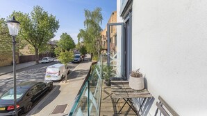 Une rue étroite, bordée de voitures garées, et un immeuble doté d’une porte en verre et d’un balcon.